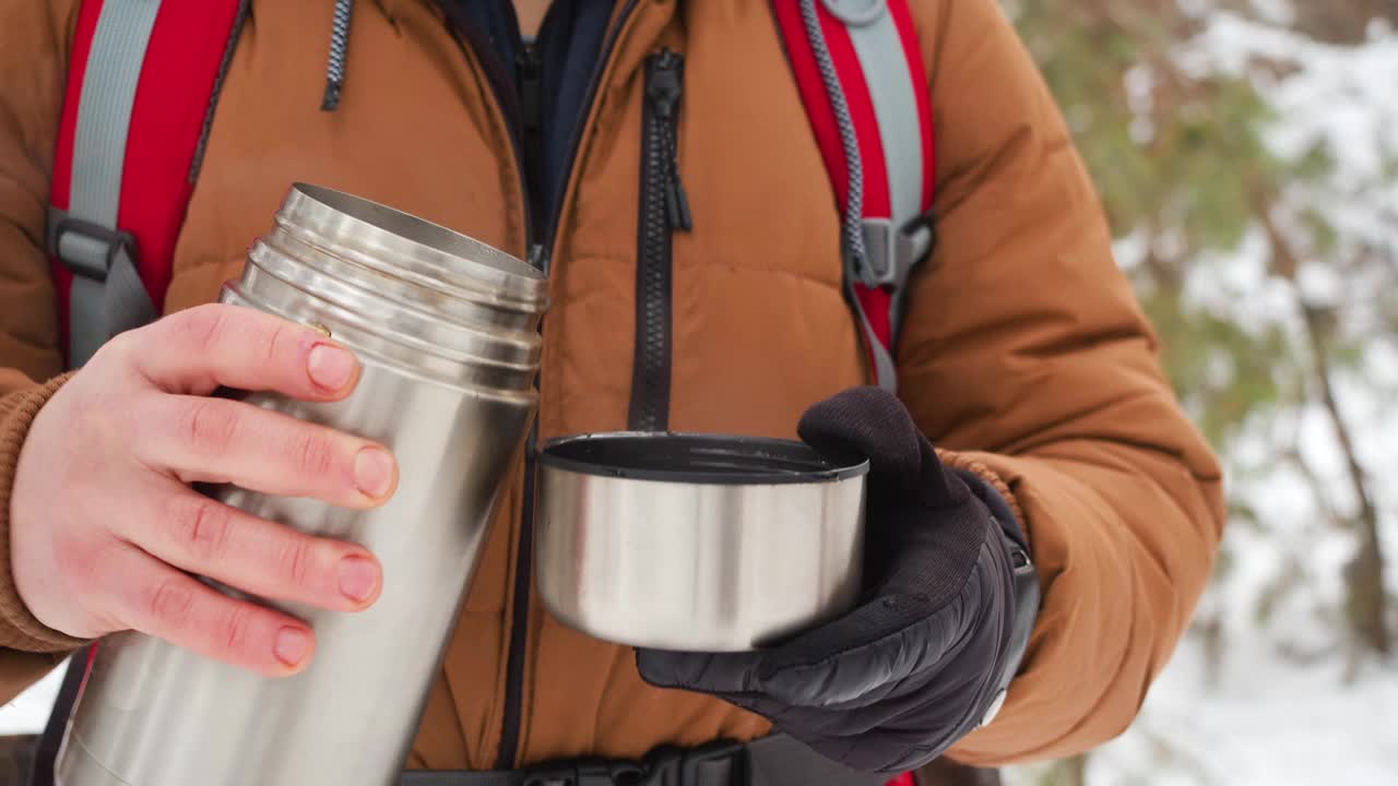 在冬天的森林里休息时，男人们用手从保温杯里倒茶。视频素材