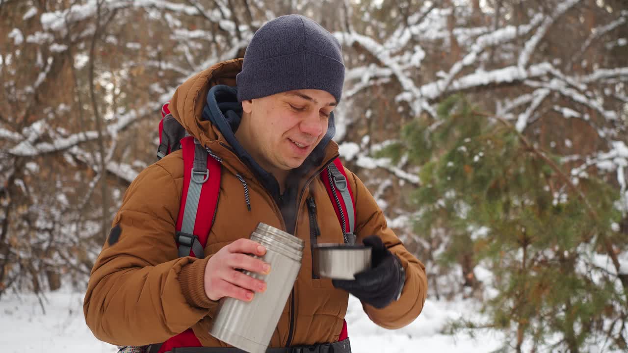 40岁的老人在冬天的雪林里徒步旅行时喝茶。视频素材