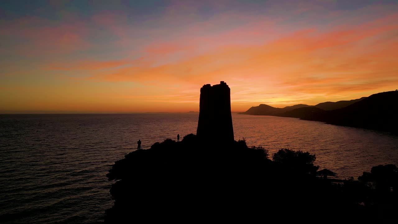 人们走在海边的悬崖上，夕阳下的红色天空。飞过瞭望塔。视频素材