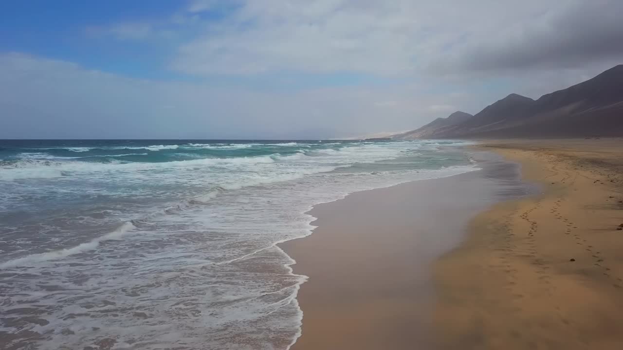 在西班牙加那利群岛富埃特文图拉的Jandia半岛，低空飞过的海浪拍打着普拉亚·德·科费特沙漠沙滩视频素材