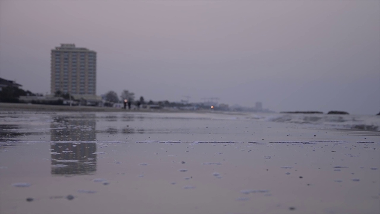 一个有许多楼层的酒店的剪影，在夜晚的门槛上，海水覆盖着海滩，沐浴在细沙上视频素材