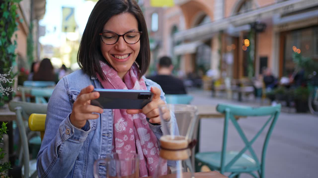 Young woman taking photos of her coffee in a sidewalk café视频素材