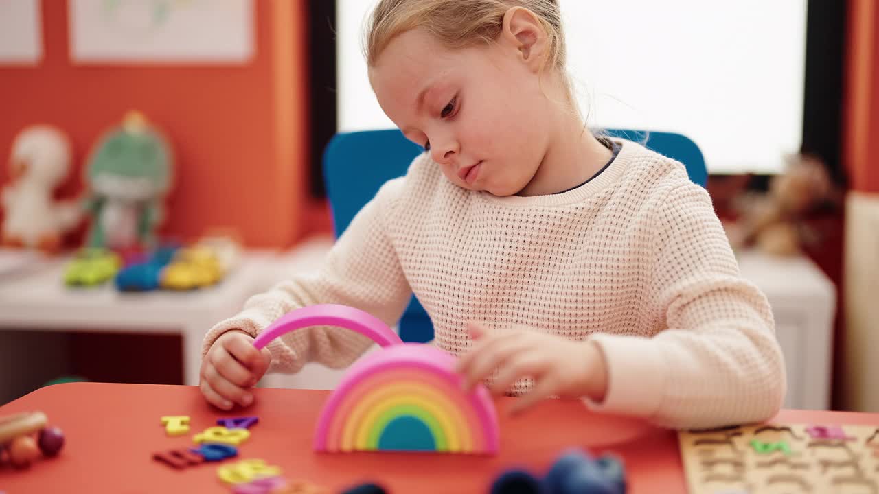 可爱的金发女孩坐在幼儿园的桌子上玩玩具视频素材