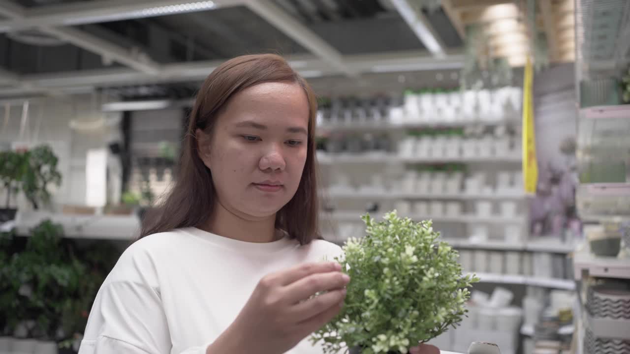 年轻女子购买盆栽植物。寻找室内植物装饰视频素材