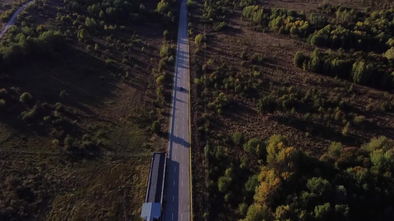 无人机拍摄到一辆汽车在田地之间的沥青公路上行驶视频素材