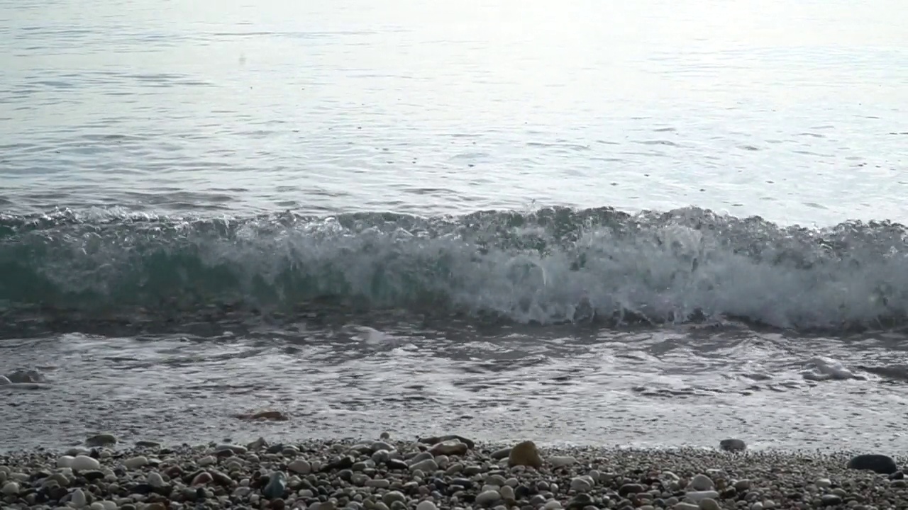 小浪，平静的水面和卵石海岸。慢动作视频素材