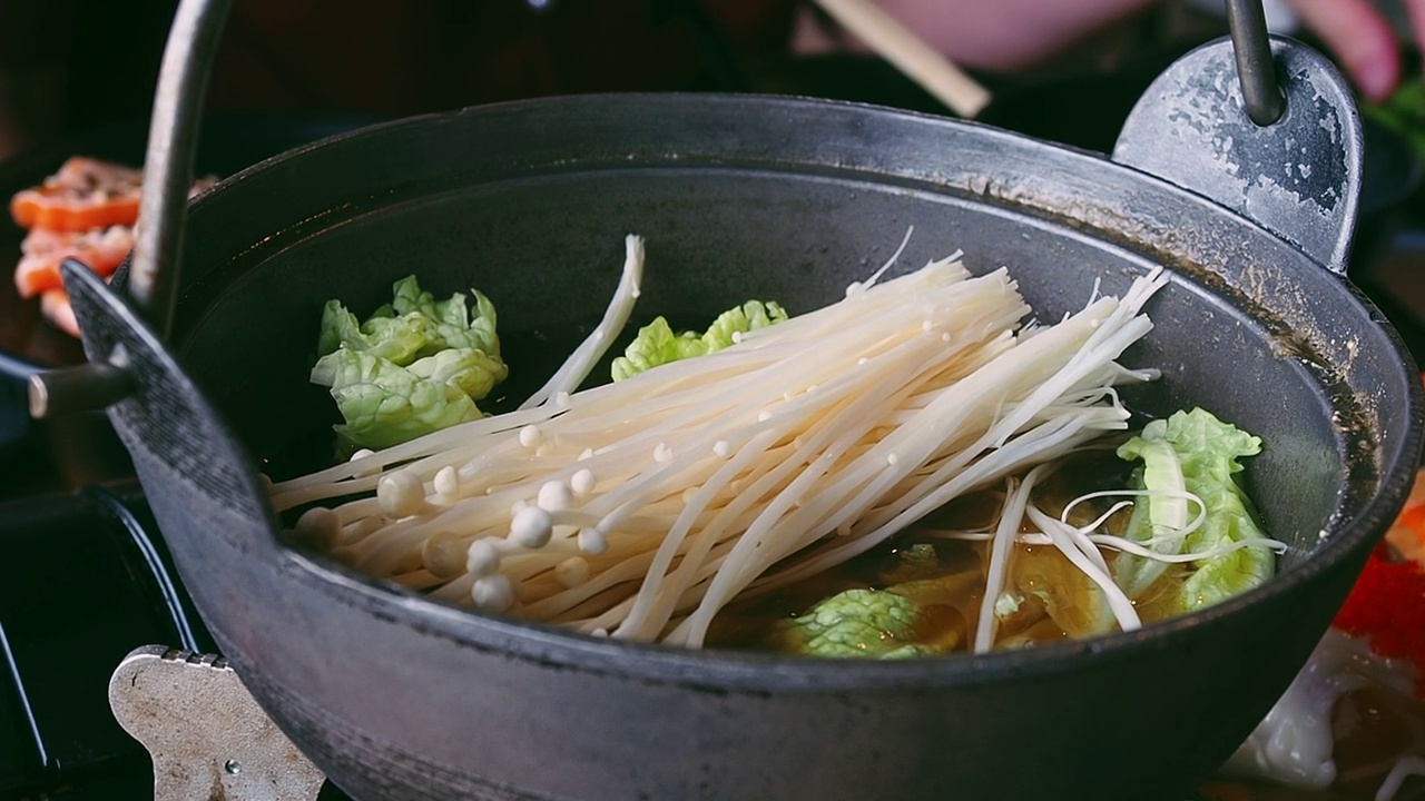 在日本餐馆里，女人用手把金针菇(金针菇或冬菇)放在涮锅里涮锅。喜欢吃火锅涮锅和寿喜烧。视频素材