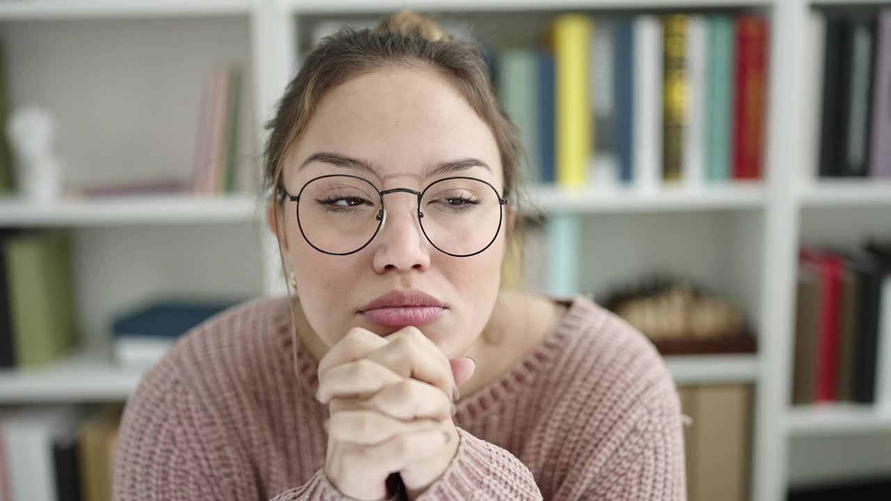 年轻美丽的西班牙女学生坐在桌子上，疑惑的表情在图书馆大学视频素材