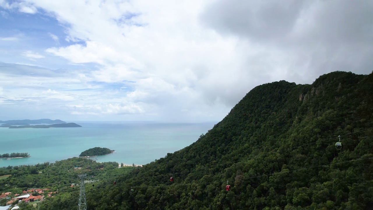 平静的蓝色海洋全景，缆车在马来西亚兰卡威岛郁郁葱葱的山脉上行驶。航盘左视频素材