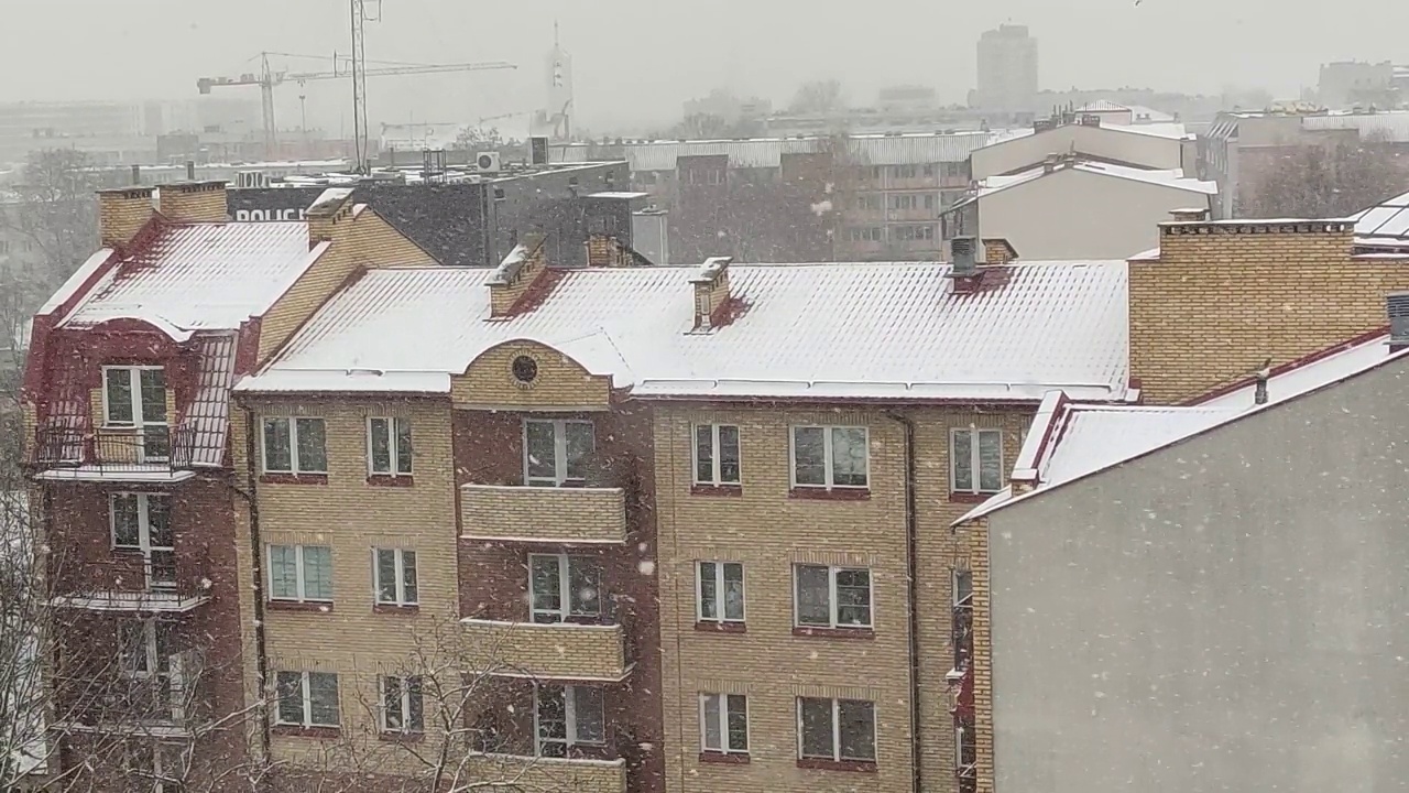 从窗户看，降雪在公寓建筑和城市景观的背景视频素材