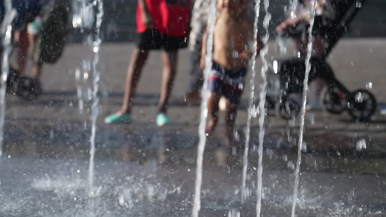 小男孩跑向喷水喷泉。夏天，孩子们在水上乐园玩耍视频素材