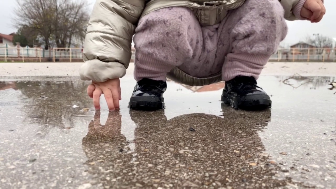 一个穿着黑靴子的孩子在水坑里跳视频素材