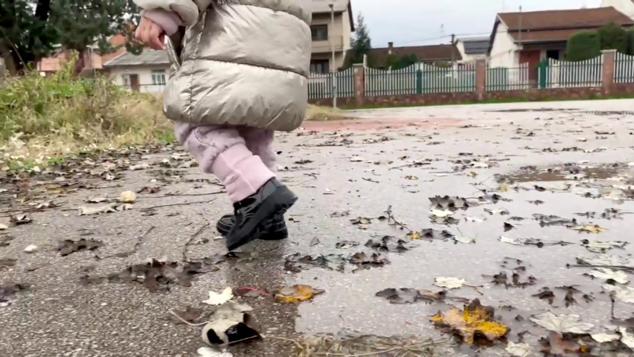 一个穿着黑靴子的孩子在水坑里跳视频素材