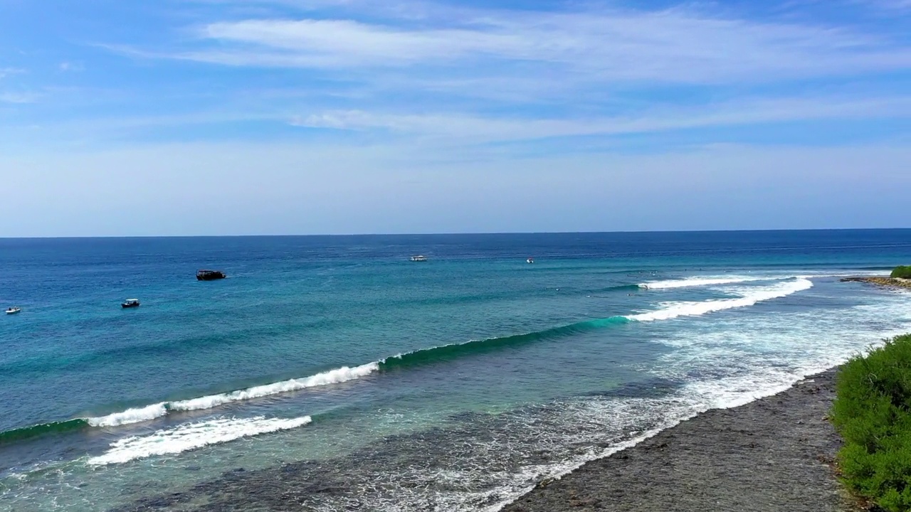 在阳光明媚的日子里，游客在天空下的海浪上冲浪的空中向前拍摄-马尔代夫的thulushoo视频素材