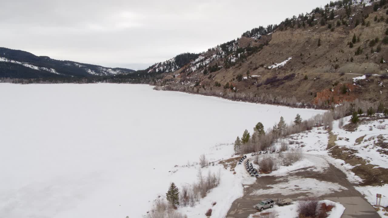 空中平移拍摄的汽车滑雪车辆停在雪覆盖的土地在云下的山脉-杰克逊，怀俄明州视频素材