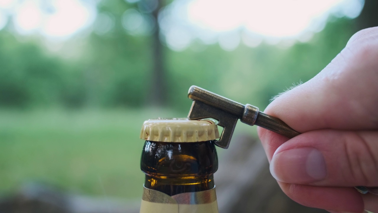 女性手打开一瓶啤酒。特写，大自然中有绿色树叶的瓶口。第一次就不行。视频素材