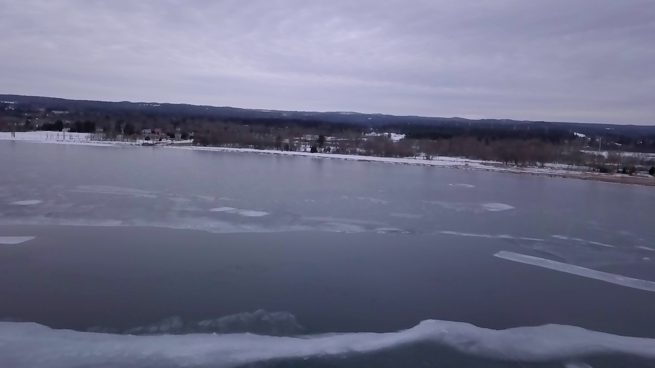 空中风景拍摄的森林在雪景，无人机飞行在云下冰冻的湖-马凯特，密歇根州视频素材