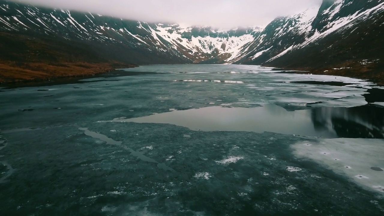 航拍:白雪覆盖的宁静山脉的田园风光，无人机在冬天飞过湖面上的冰——挪威的特罗姆瑟视频素材