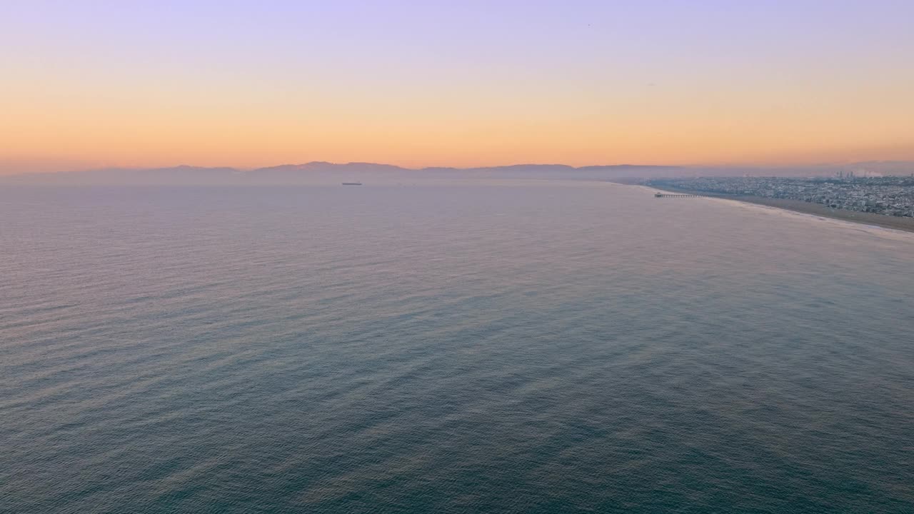 在加利福尼亚州赫莫萨海滩，宁静的海洋与山脉的背景下降的空中拍摄视频素材