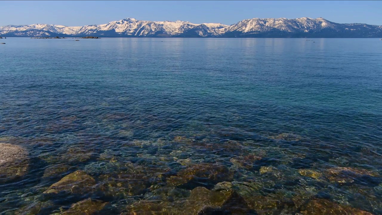 太浩湖——太浩湖清澈湛蓝的湖水特写，地平线上高耸的内华达山脉积雪覆盖的山峰。太浩湖，加利福尼亚州，美国。视频素材