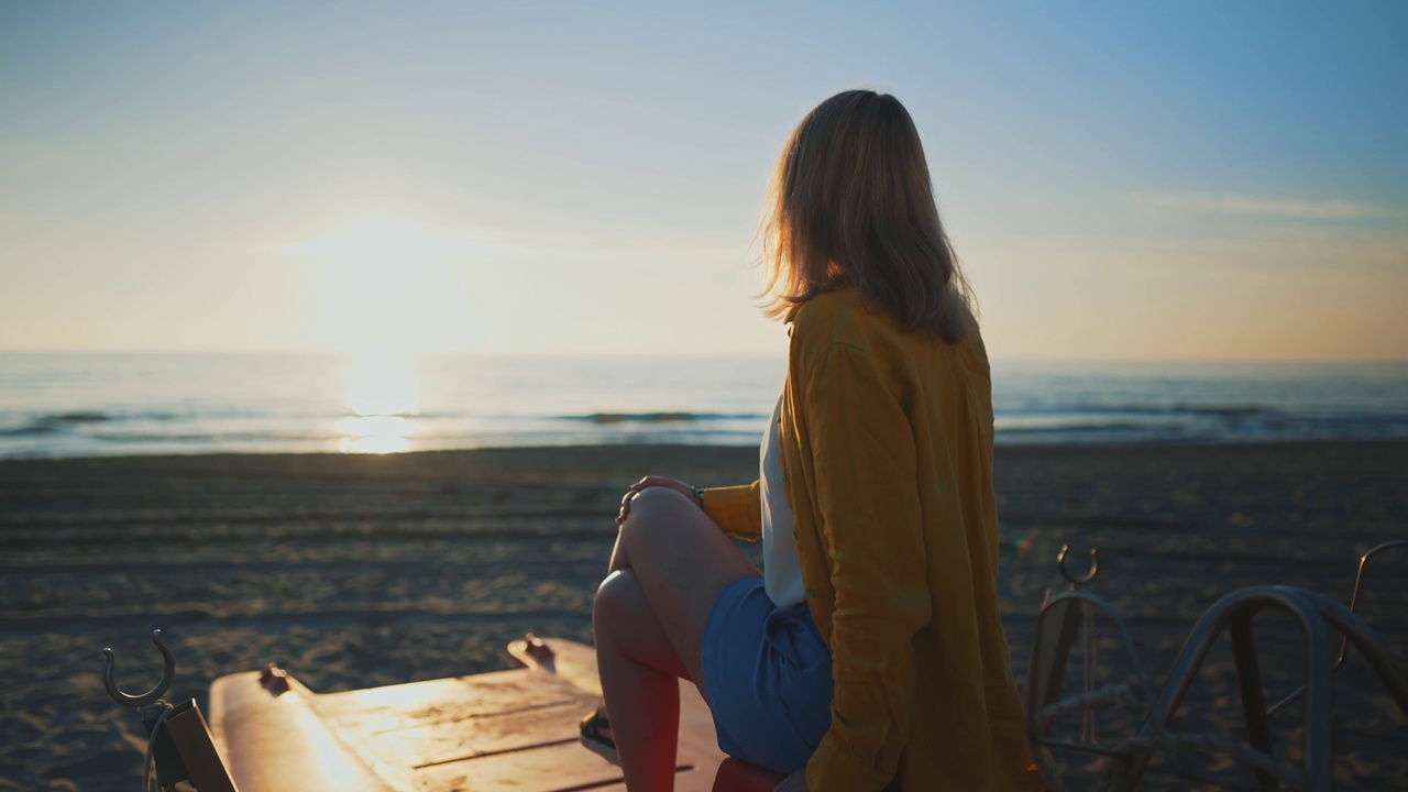 一个女人坐在船上，看着日落时分的大海。视频素材