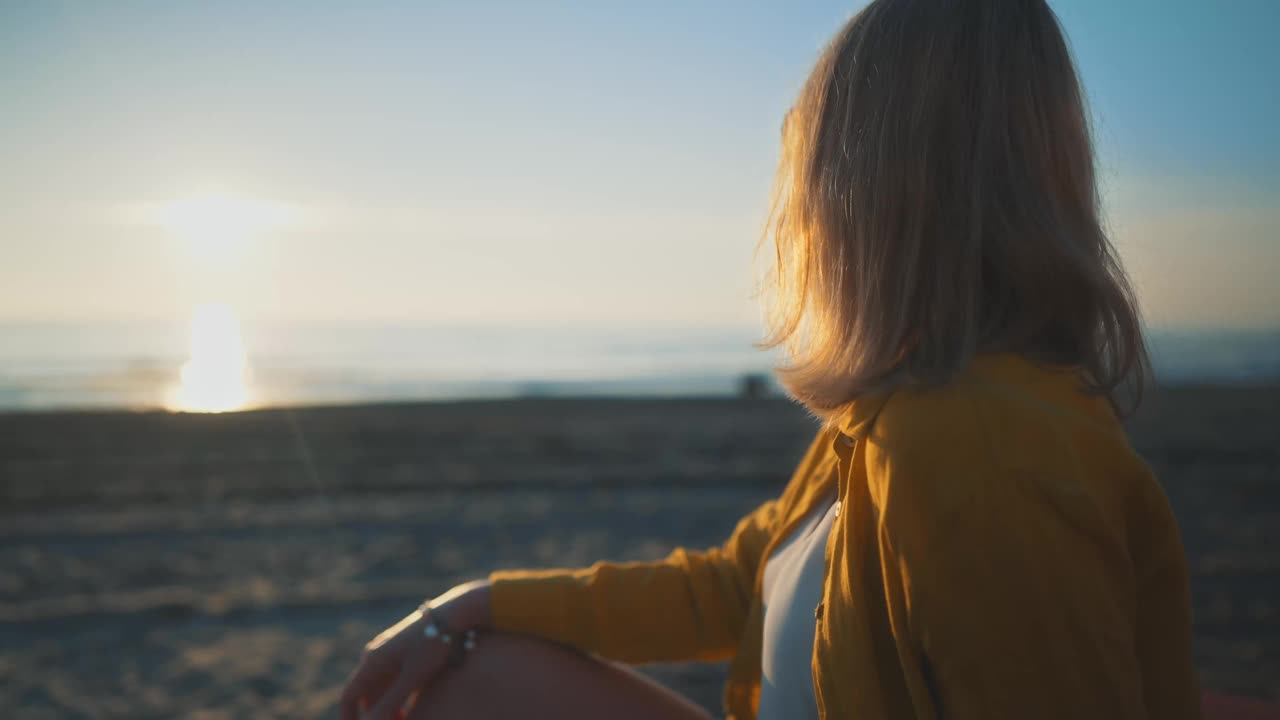 一个女人坐在船上，看着日落时分的大海。视频素材