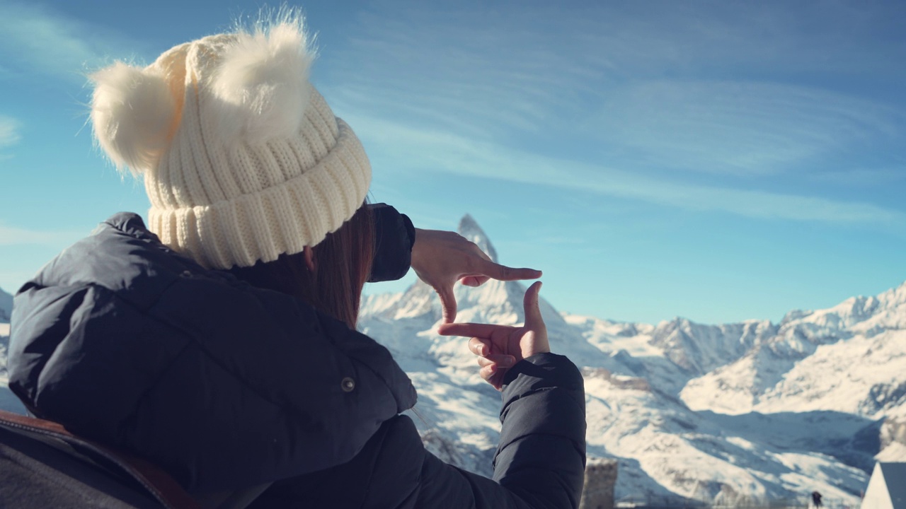 年轻的旅行者女孩站在雪峰上，与瑞士马特洪峰用手做画框的背影，冬季旅行的场景和规划。视频素材