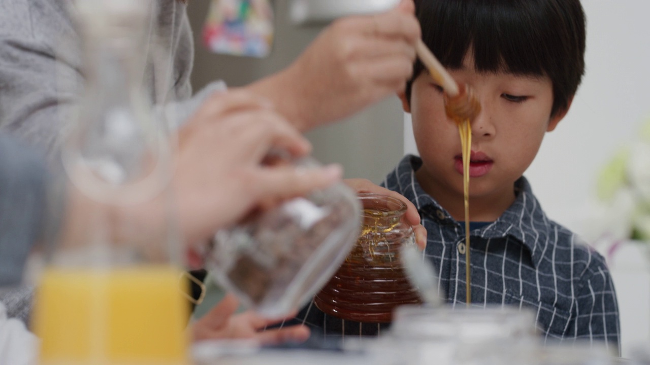 亚洲家庭正在吃早餐，妈妈为小男孩在煎饼上浇蜂蜜，妈妈为孩子们准备自制的饭菜视频素材