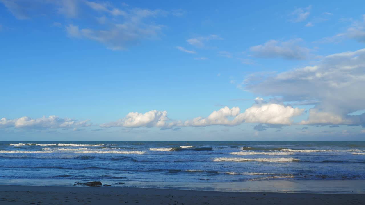 巨大的海浪拍打着沙滩。蔚蓝的天空和蓬松的白云映衬着海景。强大的海浪到达海岸，打破并产生白色的泡沫。美丽的海洋景观视频素材