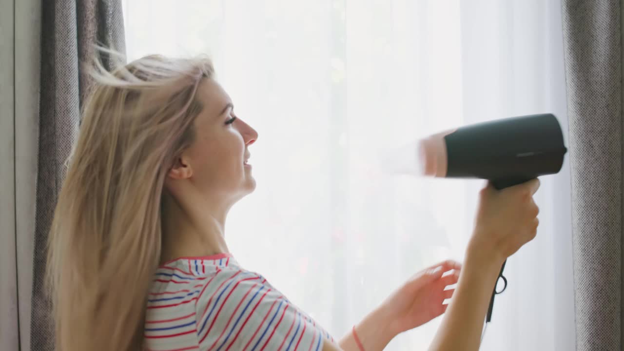 一位年轻女子用电吹风吹干她的长发。美容护发理念视频素材