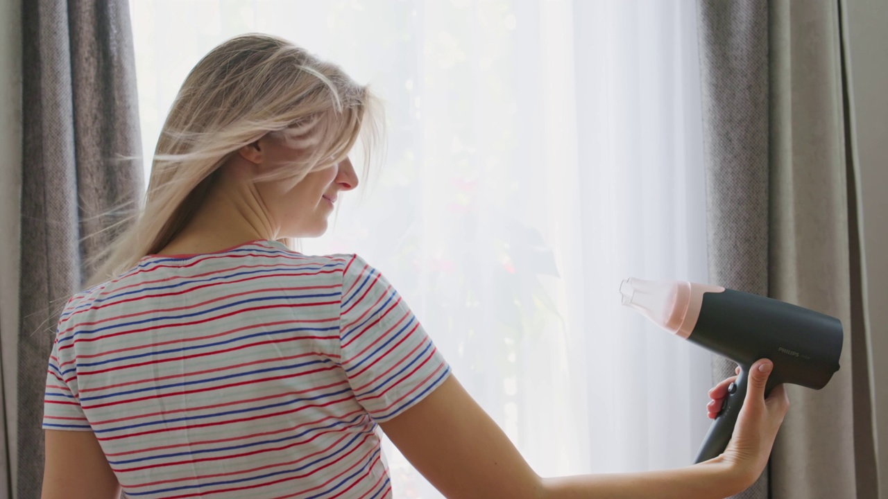 一位年轻女子用电吹风吹干她的长发。美容护发理念视频素材