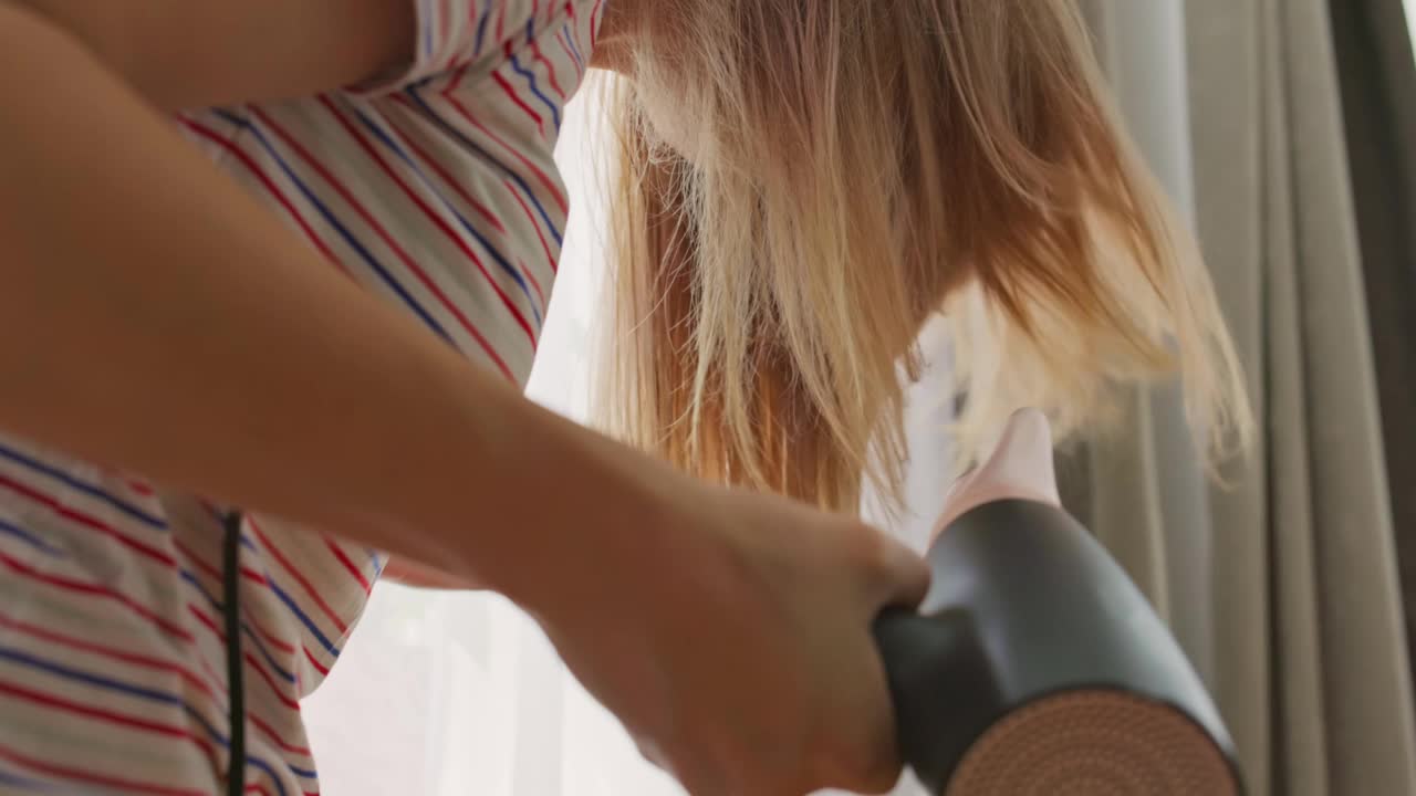 一位年轻女子用电吹风吹干她的长发。美容护发理念视频素材