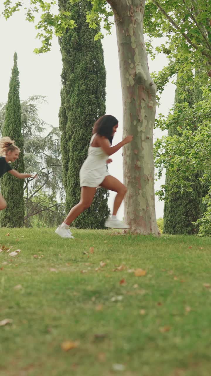 垂直视频:三个少女朋友在公园里玩捉人游戏。三个女孩朋友十几岁玩你的最后一个游戏视频素材