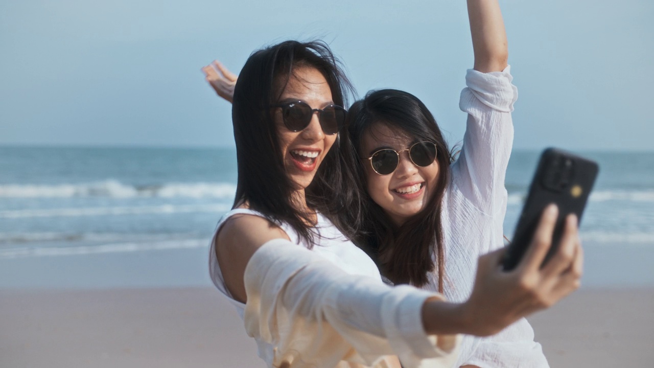 年轻的亚洲女性朋友一起在海滩上自拍。夏日出游的人们，手机智能手机拍照技术，还是快乐女人的生活理念视频素材