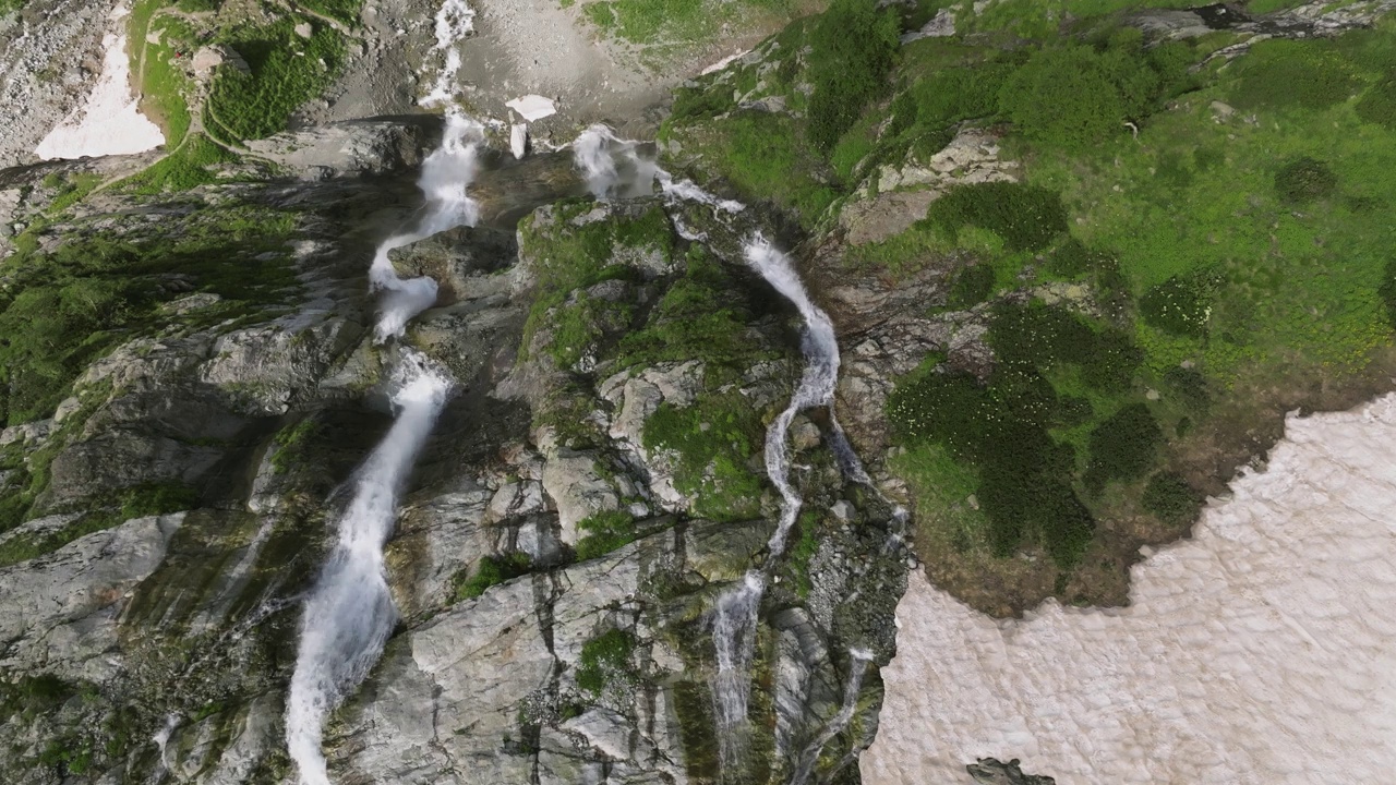 鸟瞰近距离飞行与山脉瀑布从冰川上流过岩石。视频素材