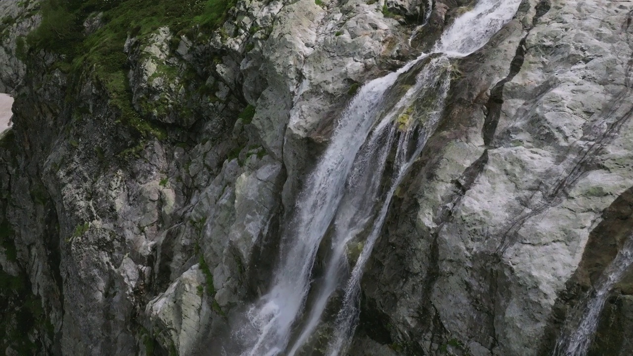 鸟瞰近距离飞行与山脉瀑布从冰川上流过岩石。视频素材