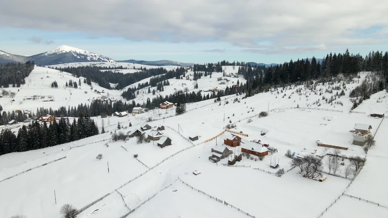 在寒冷的山区，白雪覆盖的森林之间有小村庄的冬季景观视频素材