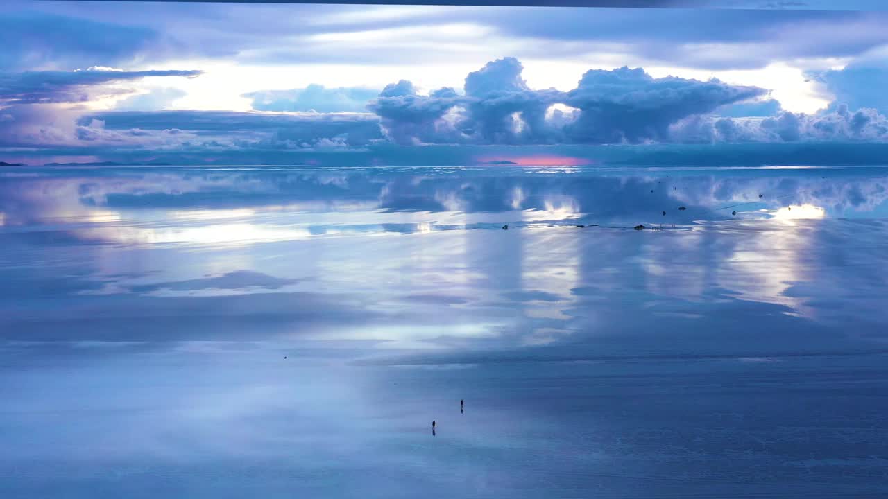 在玻利维亚雨季的深夜，一对夫妇在乌尤尼盐沼镜面般的海面上行走。视频素材