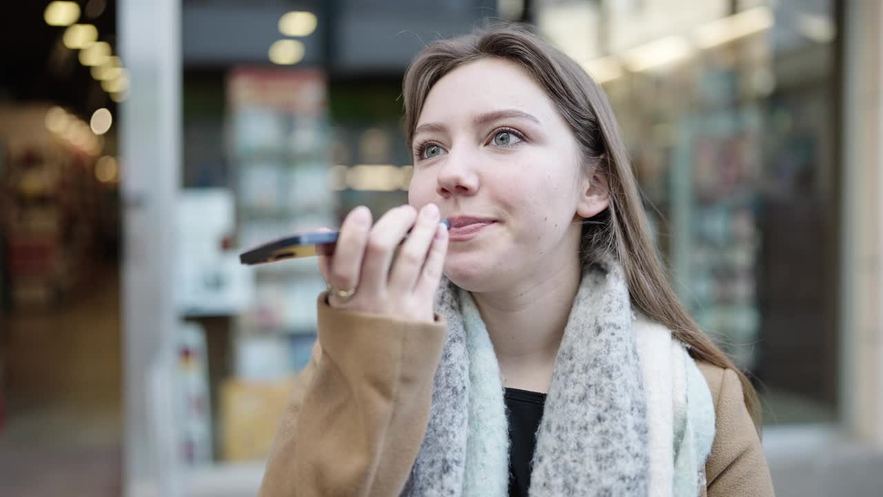 年轻的金发女子微笑自信地在街上通过智能手机发送语音信息视频素材