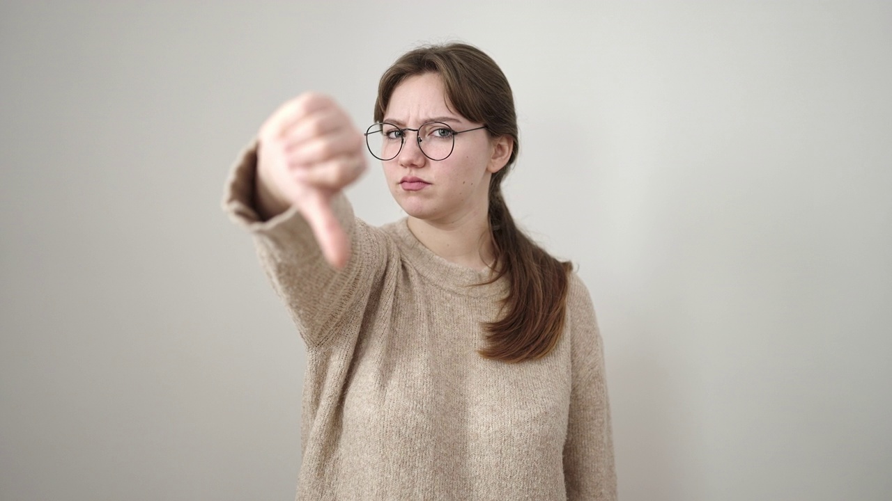 年轻的金发女子做消极的手势与拇指向下孤立的白色背景视频素材