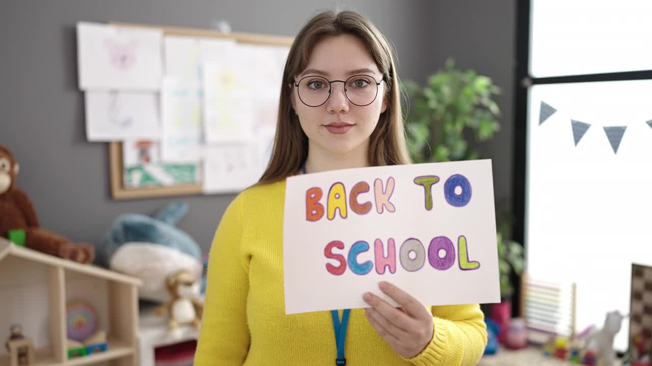 年轻的金发女幼儿园老师拿着学校的纸做来的手势在幼儿园视频素材