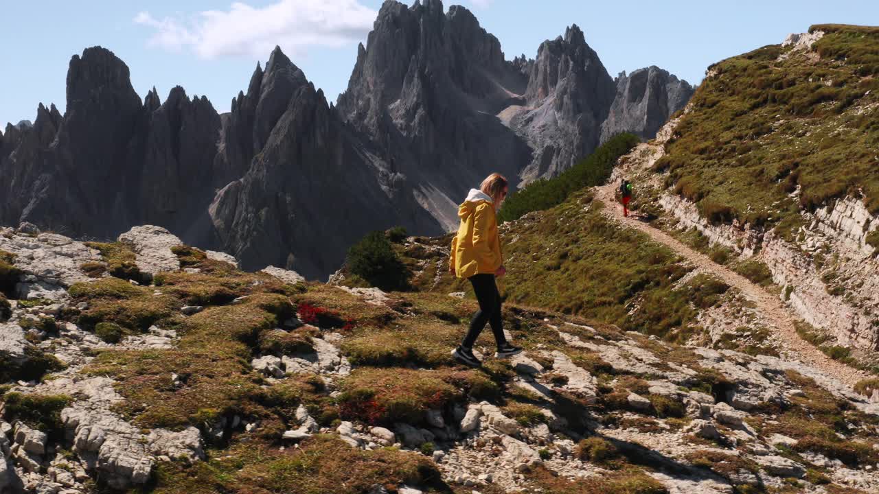 穿黄夹克的女人沿着岩石山峰下山视频素材