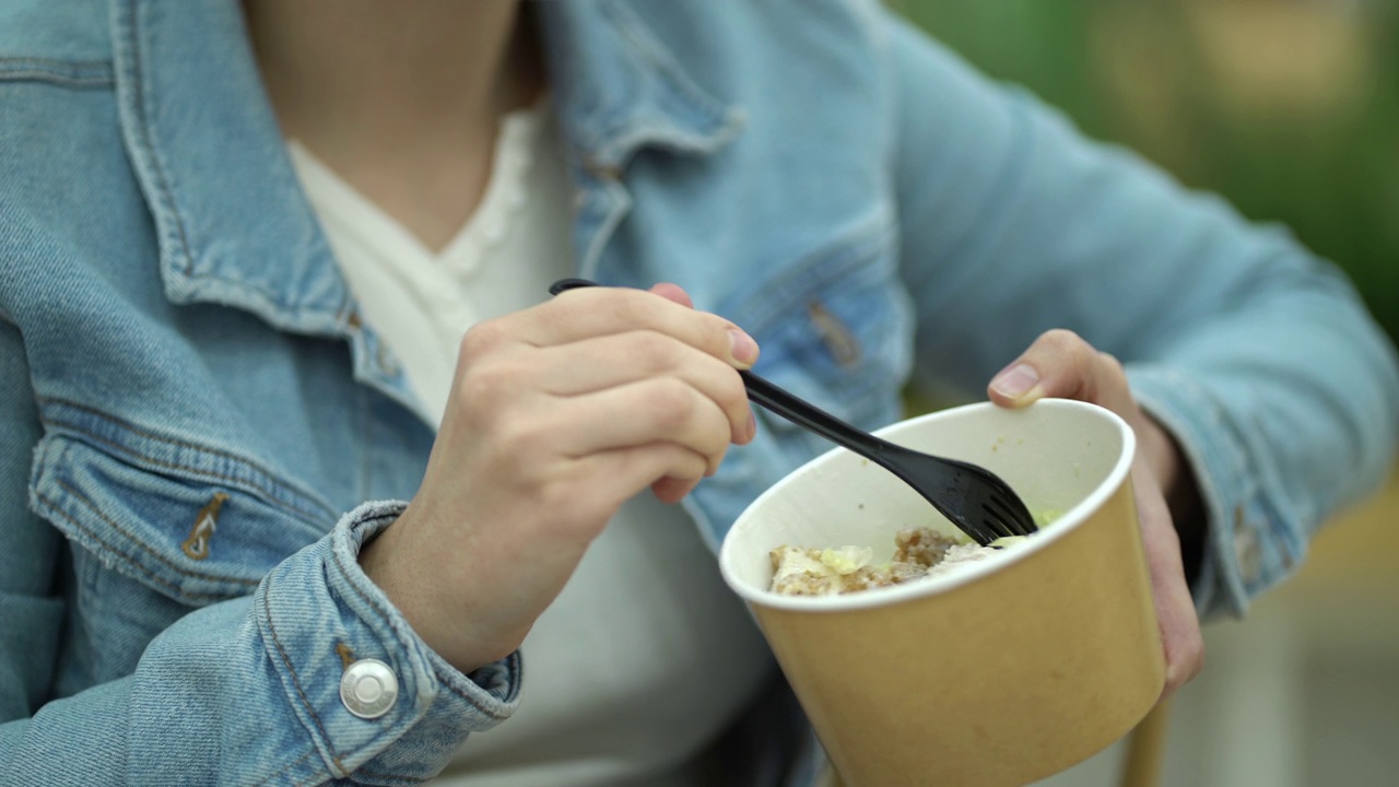 把注意力集中在纸容器上，年轻女子手里拿着凯撒沙拉。女孩在美食广场吃新鲜沙拉。视频下载