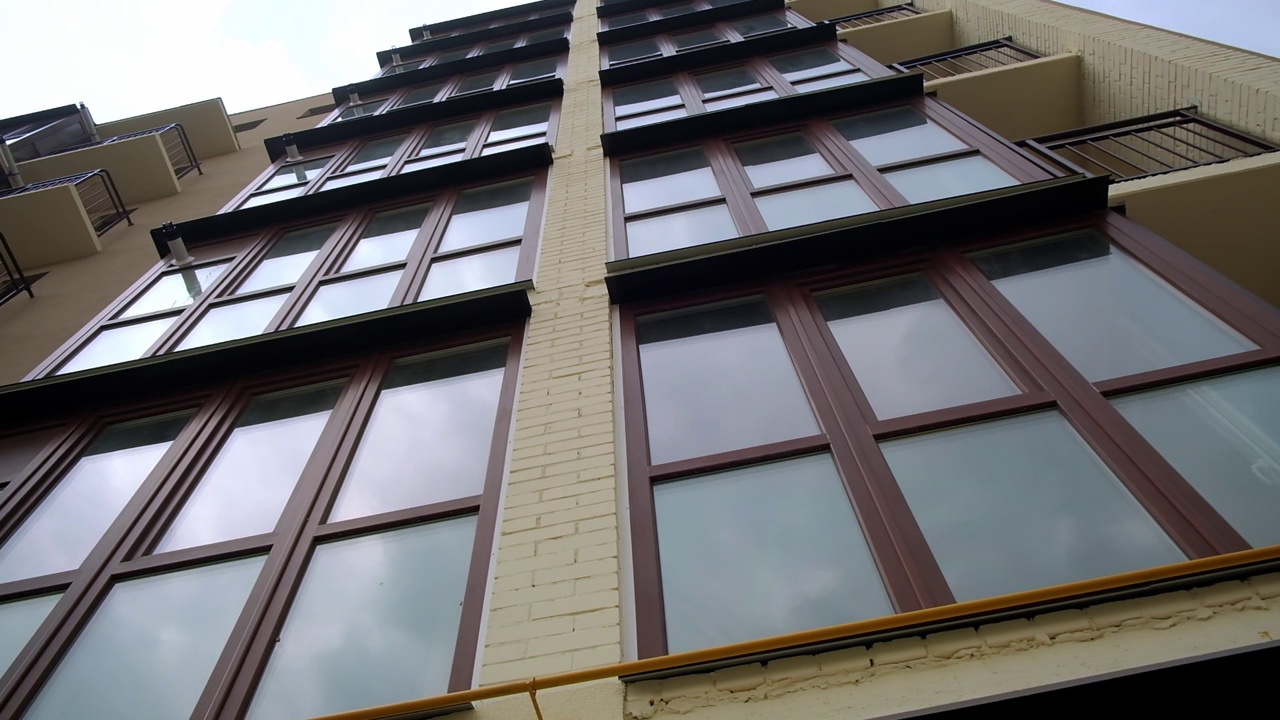 Glazed balconies and opened ones at the faзade of newly-built residential building. Contemporary housing at backdrop of grey sky. Low angle view.视频素材