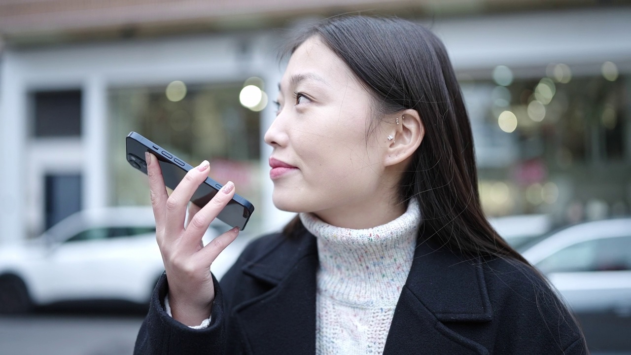 年轻的中国女子微笑着自信地在街上用智能手机发送语音信息视频素材