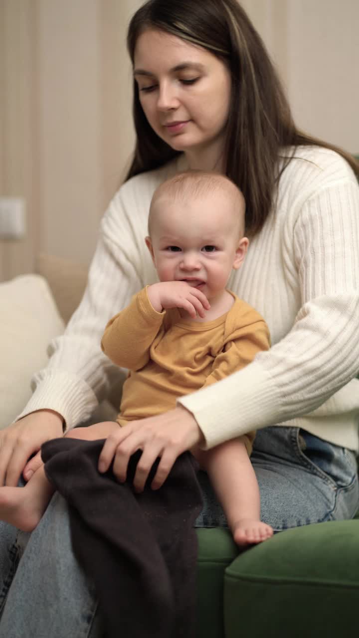 妈妈给坐在沙发上的小儿子穿上衣服。妈妈给孩子换裤子。视频下载