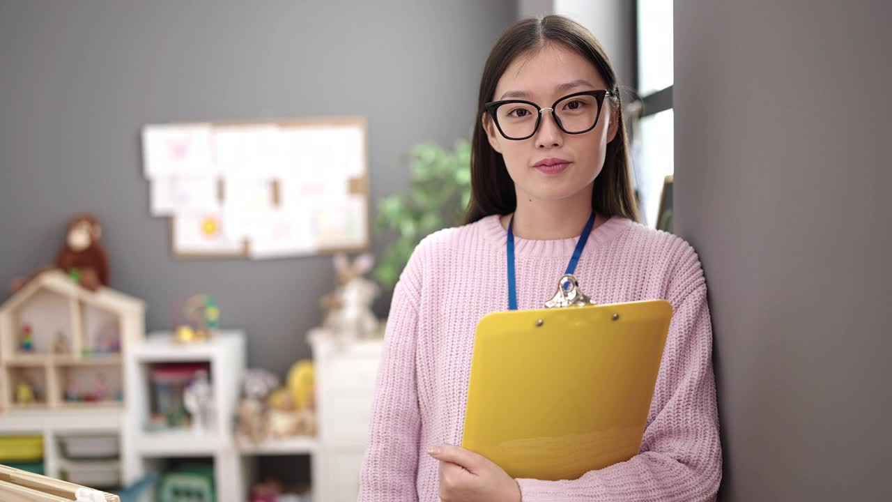 年轻的中国女幼儿教师微笑着自信地拿着剪贴板在幼儿园视频素材