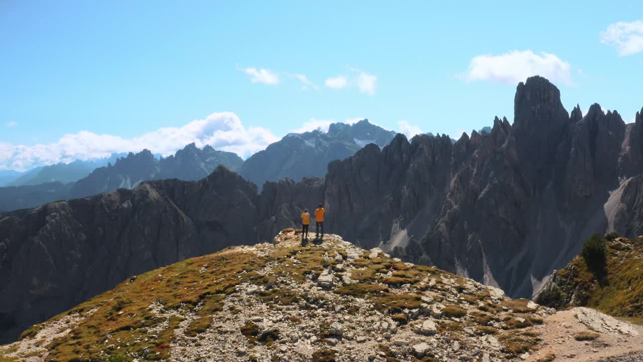 男人和女人站在阿尔卑斯山的山顶上看着岩石峰视频素材