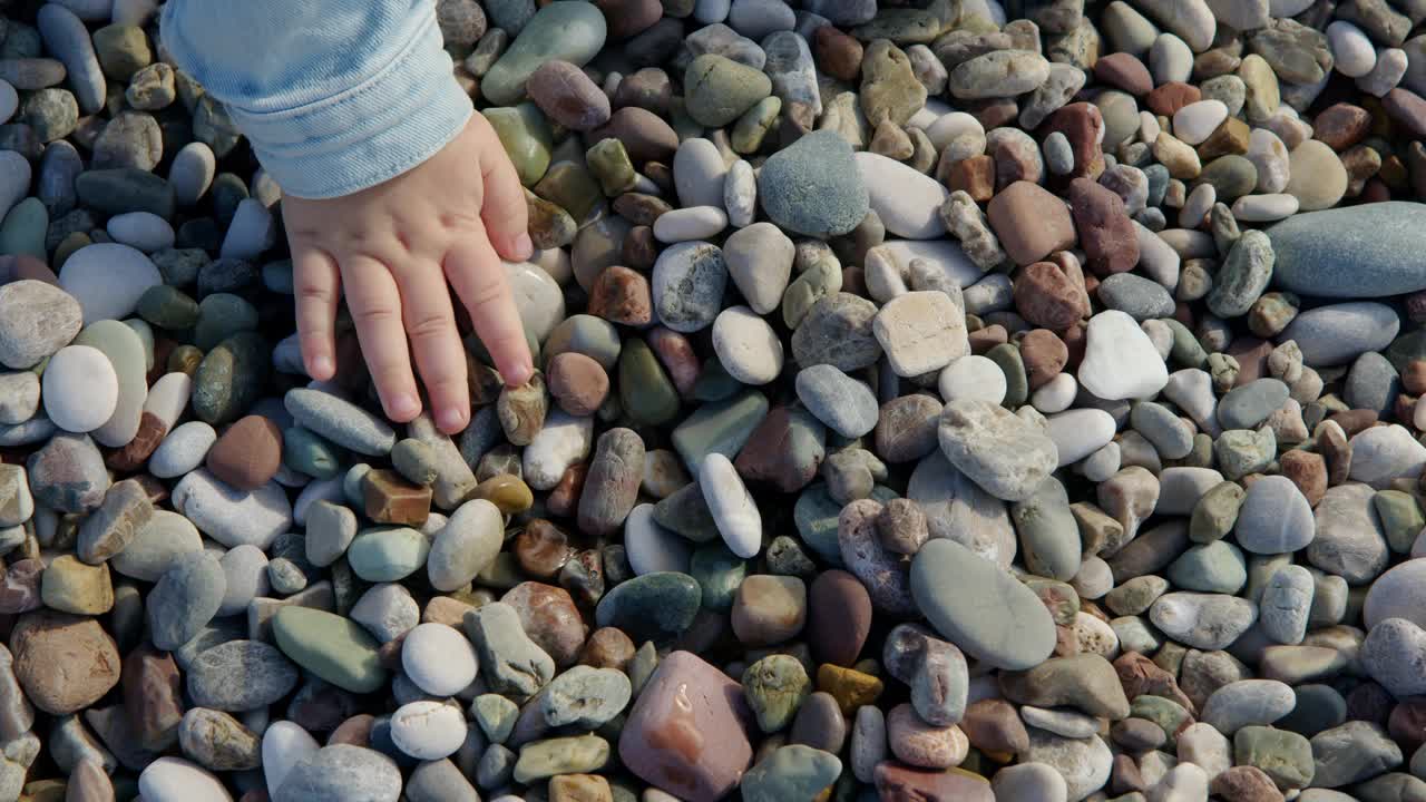 小女孩是不认识的石头海滩上玩和挖在她的手，自上而下的观点，孩子在海滩上玩。视频素材