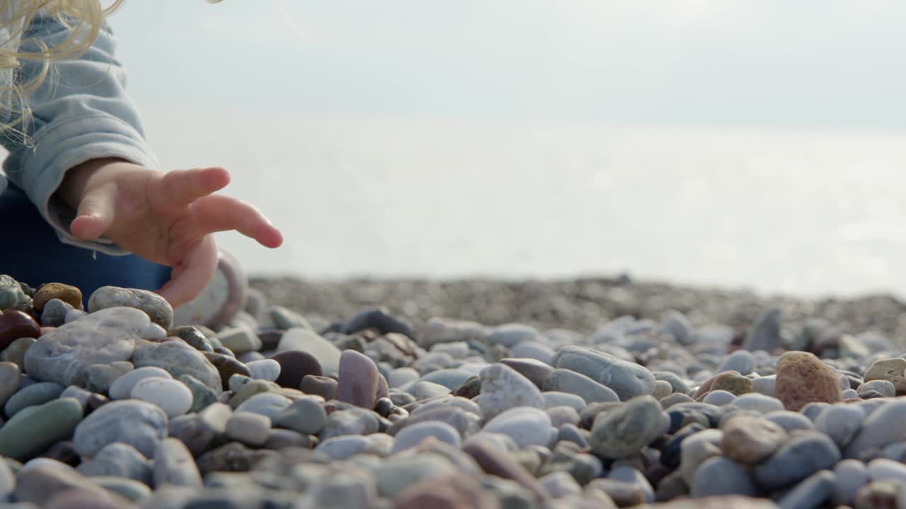 小女孩是不认识的石头海滩上玩和挖在她的手，自上而下的观点，孩子在海滩上玩。视频素材